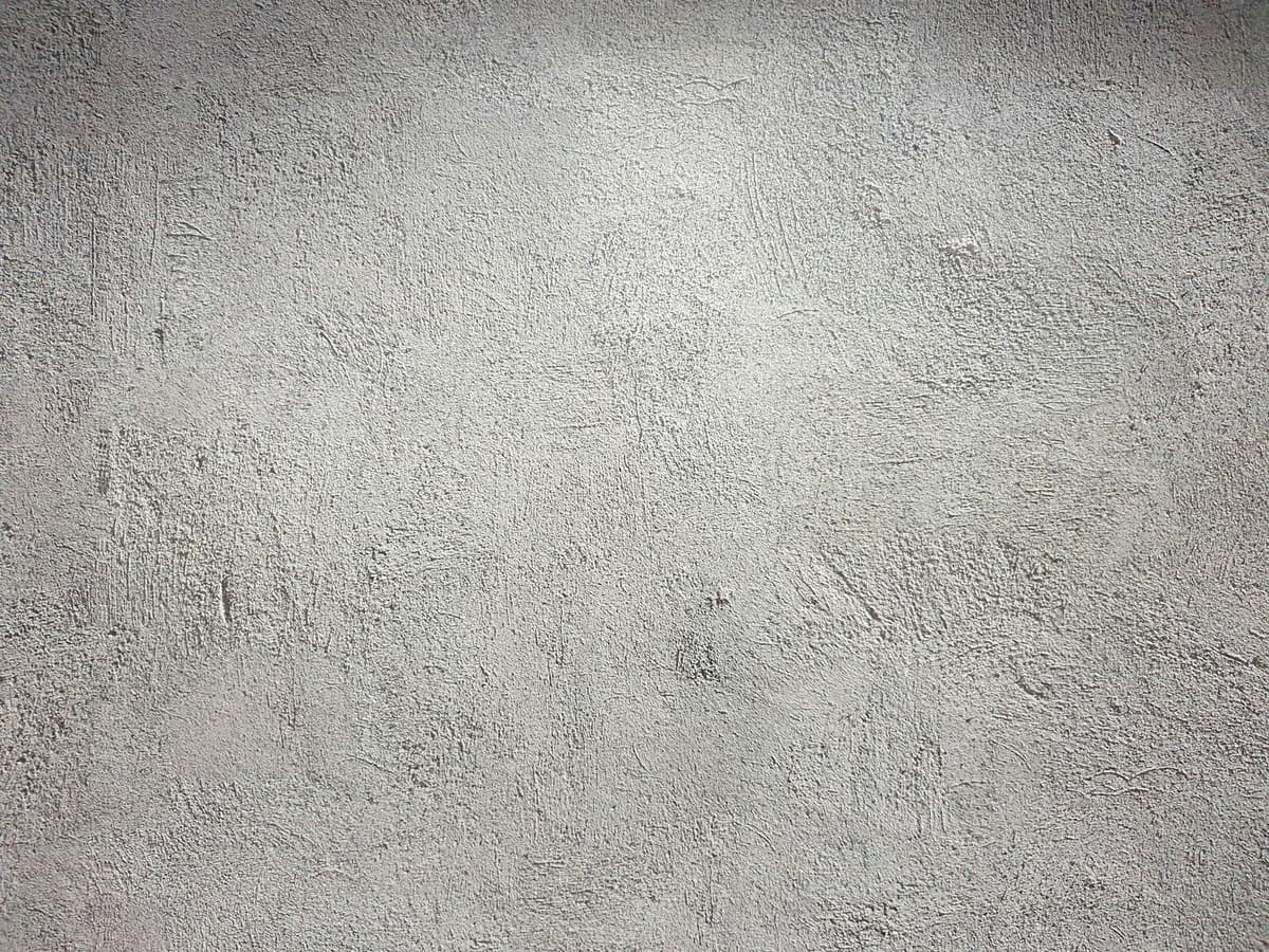 A light grey wall with a rough and uneven plaster texture